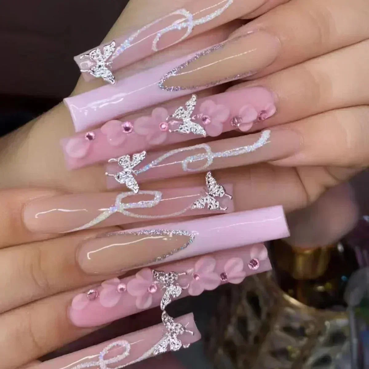 Long pink ballet false nails with butterfly rhinestones and glitter design.